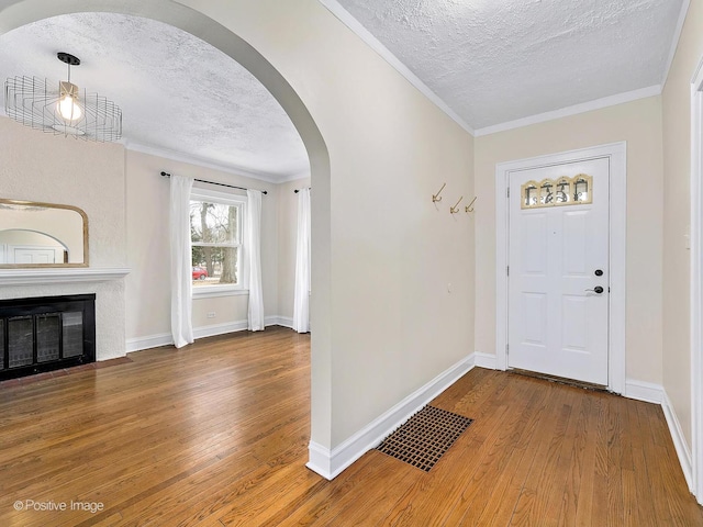 foyer featuring arched walkways, crown molding, visible vents, a fireplace with flush hearth, and hardwood / wood-style floors