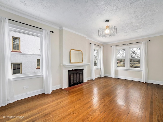 unfurnished living room featuring baseboards, a fireplace with flush hearth, ornamental molding, hardwood / wood-style floors, and a textured ceiling