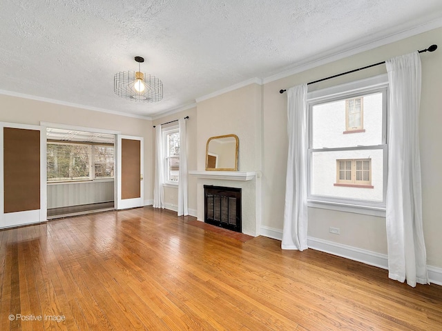 unfurnished living room with ornamental molding, a glass covered fireplace, a textured ceiling, light wood-type flooring, and baseboards