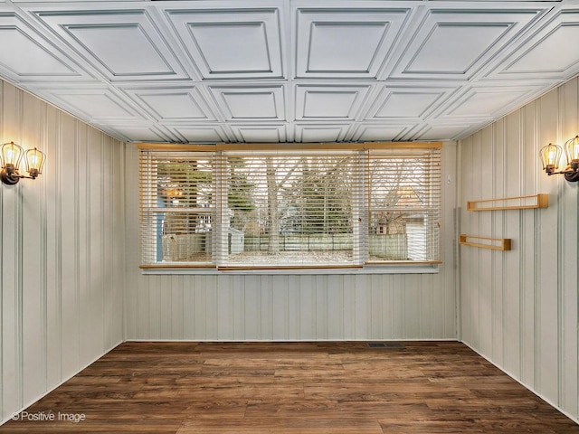 empty room featuring an ornate ceiling, wooden walls, and wood finished floors