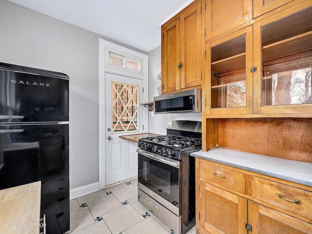 kitchen with light tile patterned floors, light countertops, appliances with stainless steel finishes, brown cabinetry, and baseboards