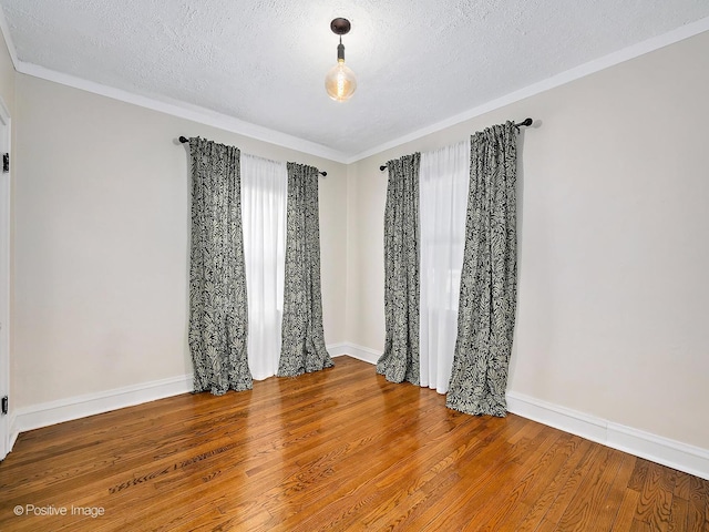 empty room with a textured ceiling, baseboards, wood finished floors, and ornamental molding