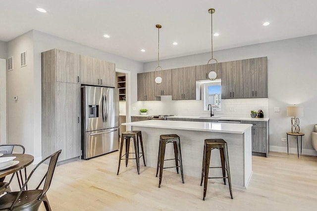 kitchen with hanging light fixtures, a kitchen breakfast bar, a center island, stainless steel refrigerator with ice dispenser, and light wood-type flooring