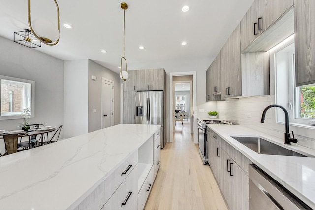 kitchen featuring pendant lighting, stainless steel appliances, light stone countertops, and sink