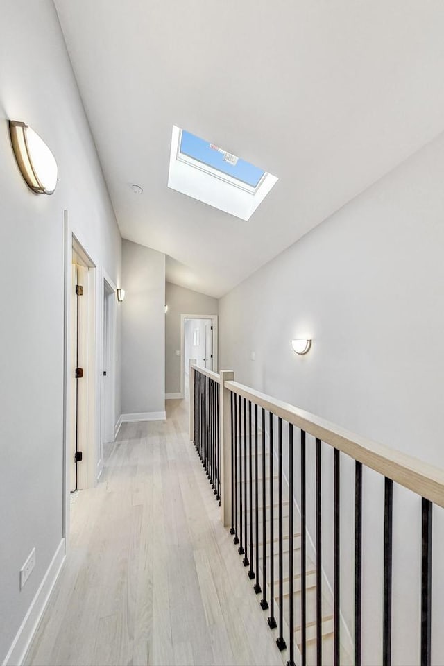 corridor featuring vaulted ceiling with skylight and light wood-type flooring