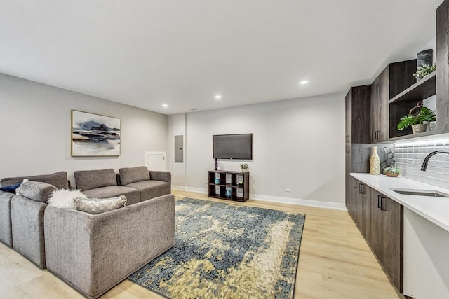 living room with electric panel, sink, and light wood-type flooring