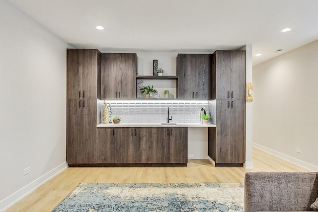 interior space with light wood-type flooring, sink, backsplash, and dark brown cabinetry