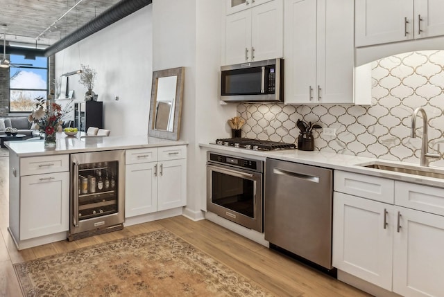 kitchen featuring a sink, appliances with stainless steel finishes, beverage cooler, white cabinetry, and light wood-type flooring