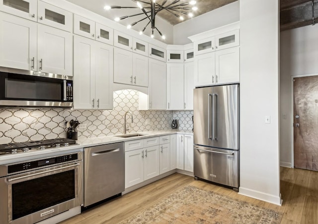 kitchen with glass insert cabinets, a sink, white cabinetry, light countertops, and appliances with stainless steel finishes