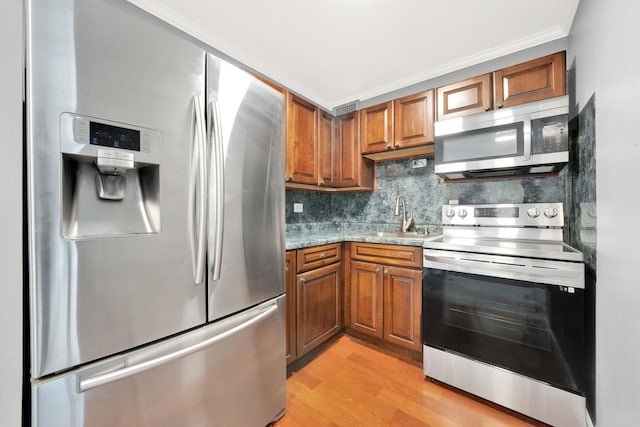 kitchen with sink, light stone counters, light wood-type flooring, stainless steel appliances, and decorative backsplash