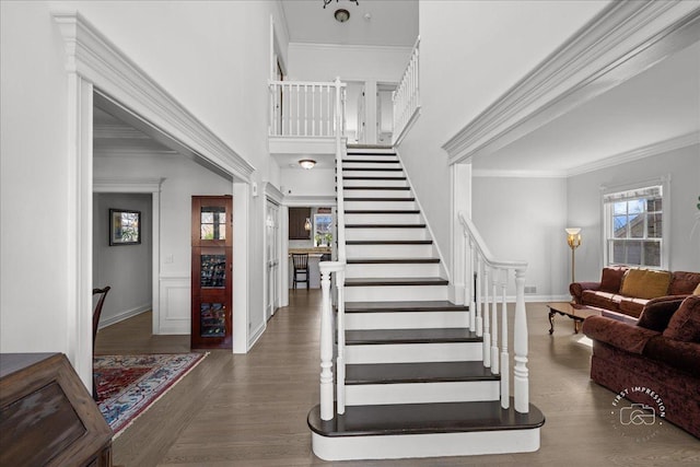 staircase with baseboards, crown molding, a high ceiling, and wood finished floors