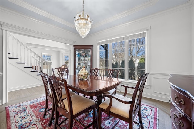 dining room featuring stairway, ornamental molding, wainscoting, an inviting chandelier, and a decorative wall