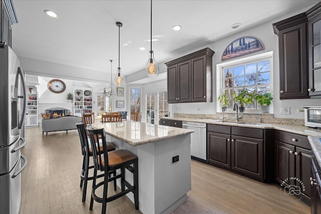 kitchen with a large fireplace, dark brown cabinetry, open floor plan, appliances with stainless steel finishes, and a sink