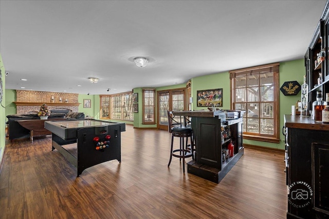 playroom featuring baseboards, a brick fireplace, a dry bar, and dark wood-style flooring