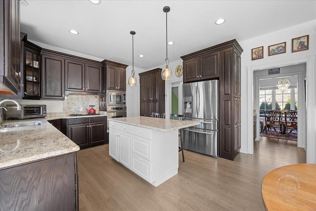 kitchen with dark brown cabinets, pendant lighting, light wood-style flooring, stainless steel appliances, and a sink