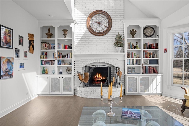 living area featuring built in shelves, wood finished floors, baseboards, lofted ceiling, and a fireplace