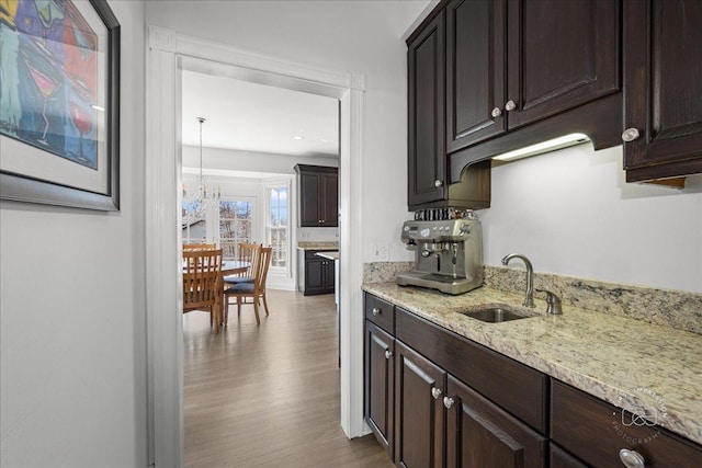 kitchen featuring light stone counters, dark brown cabinets, wood finished floors, and a sink