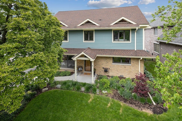 traditional-style home with brick siding, roof with shingles, a patio area, and a front yard