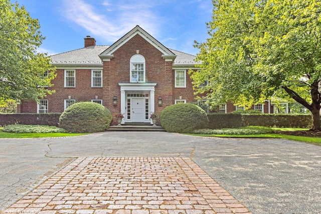 georgian-style home with driveway, brick siding, and a chimney