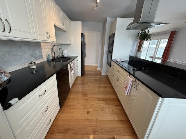 kitchen featuring dark countertops, light wood finished floors, island exhaust hood, black appliances, and a sink