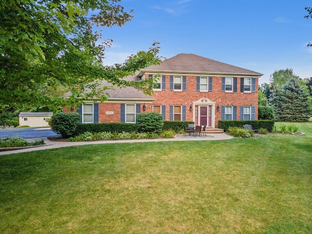 colonial house featuring a patio, a front lawn, and brick siding