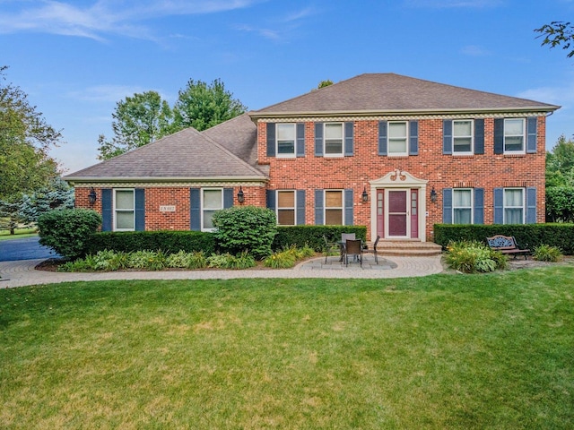 colonial-style house with a front yard, brick siding, and roof with shingles