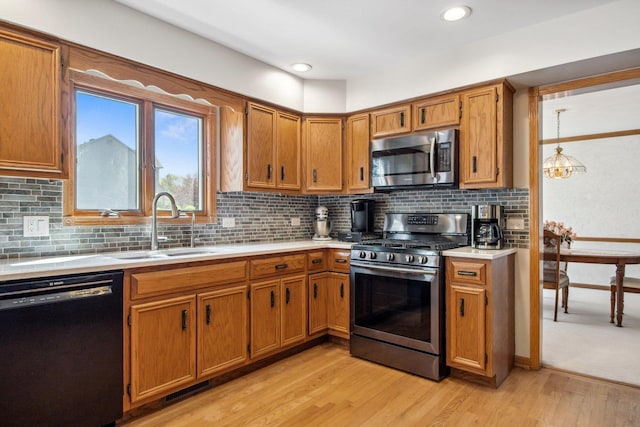 kitchen with appliances with stainless steel finishes, brown cabinets, light countertops, light wood-type flooring, and a sink