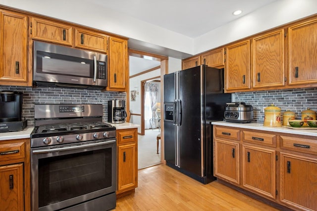 kitchen with stainless steel appliances, light countertops, light wood-type flooring, and brown cabinets