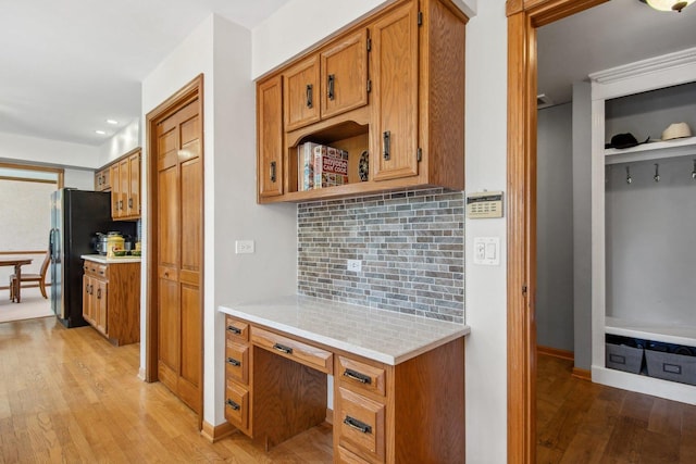 kitchen featuring decorative backsplash, freestanding refrigerator, light countertops, light wood-type flooring, and built in desk