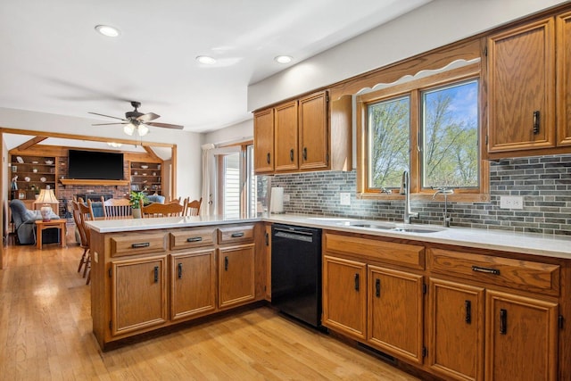 kitchen featuring black dishwasher, a peninsula, brown cabinetry, and a sink