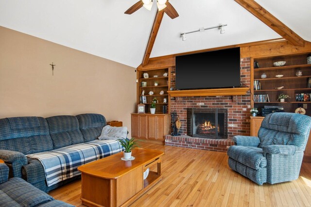 living area featuring vaulted ceiling with beams, light wood-type flooring, built in features, and a brick fireplace