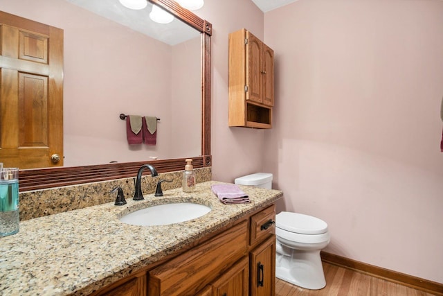 bathroom with wood finished floors, vanity, toilet, and baseboards