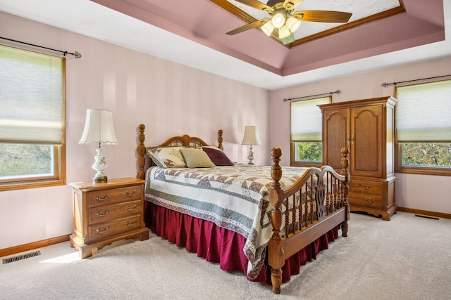 bedroom with a tray ceiling, visible vents, light carpet, and multiple windows