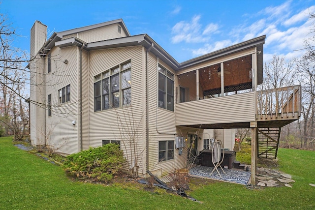 rear view of house featuring a yard, a chimney, a sunroom, ceiling fan, and stairway