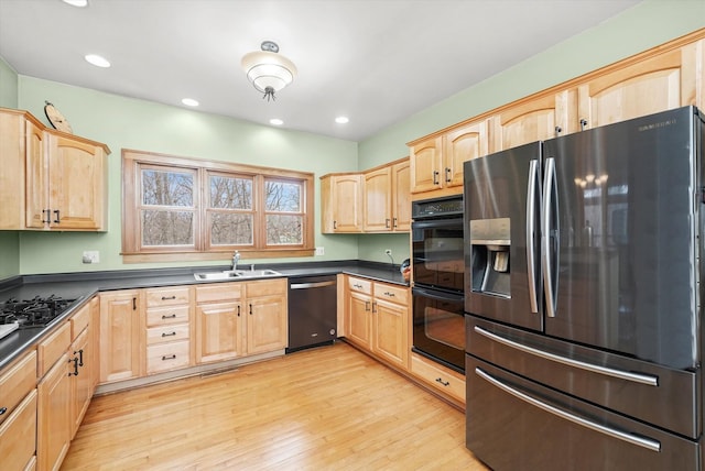 kitchen featuring black appliances, a sink, light brown cabinetry, dark countertops, and light wood finished floors