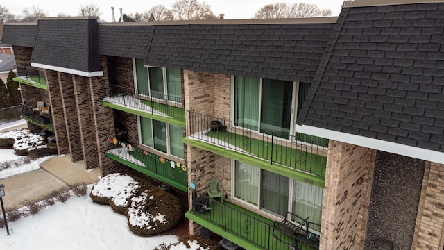 view of snowy exterior with roof with shingles and brick siding