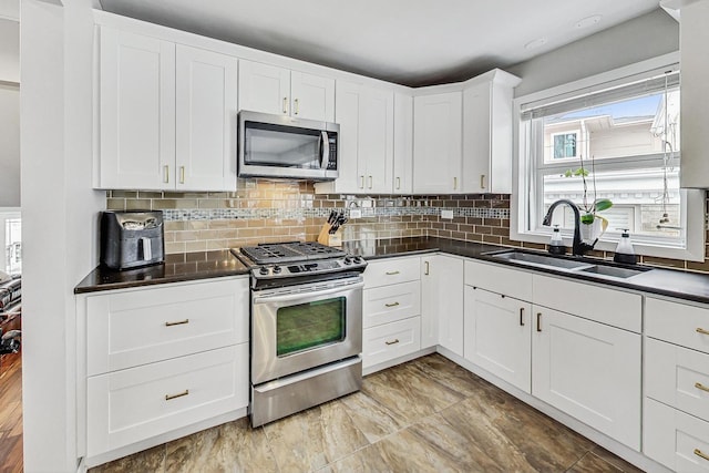 kitchen with stainless steel appliances, dark countertops, backsplash, white cabinetry, and a sink