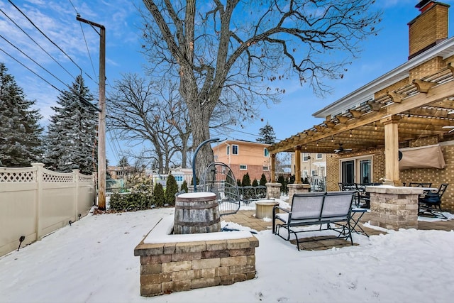 snow covered patio featuring outdoor dining area, fence, and a pergola