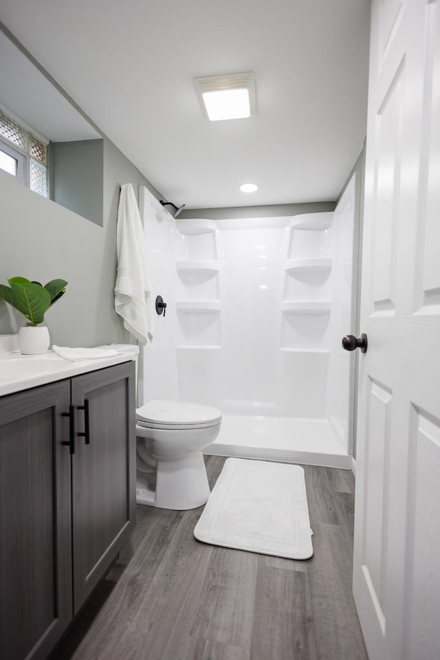 bathroom featuring hardwood / wood-style flooring, vanity, toilet, and a shower