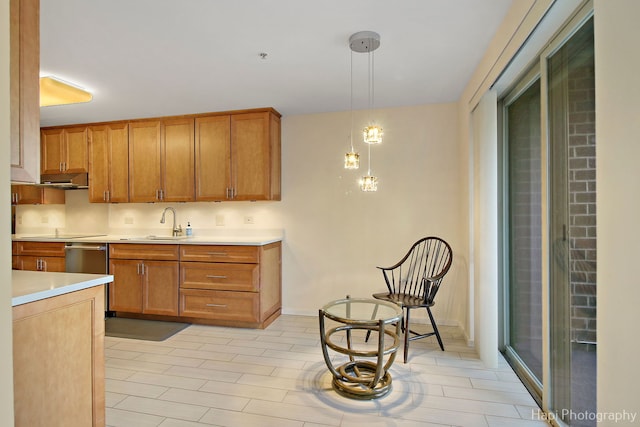 kitchen featuring brown cabinetry, light countertops, a sink, and decorative light fixtures