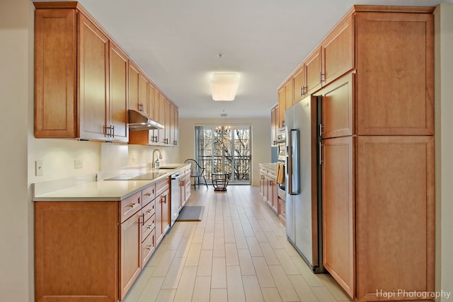 kitchen with stainless steel appliances, light countertops, light wood-style floors, a sink, and under cabinet range hood