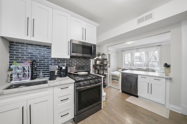 kitchen featuring light wood-type flooring, stainless steel appliances, light stone countertops, sink, and white cabinets