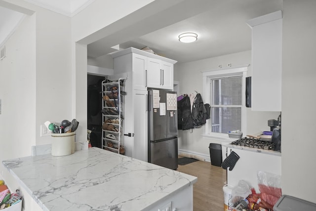 kitchen featuring white cabinets, hardwood / wood-style flooring, stainless steel fridge, and light stone counters