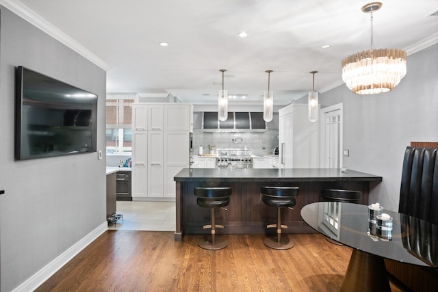 kitchen featuring stainless steel range with gas cooktop, ornamental molding, backsplash, a breakfast bar, and white cabinetry