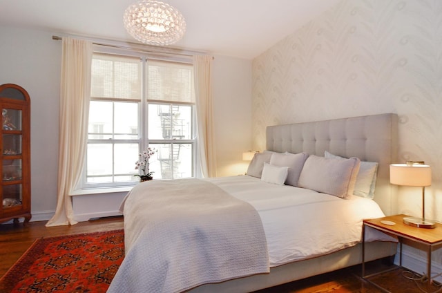 bedroom with wallpapered walls, wood finished floors, baseboards, and a chandelier