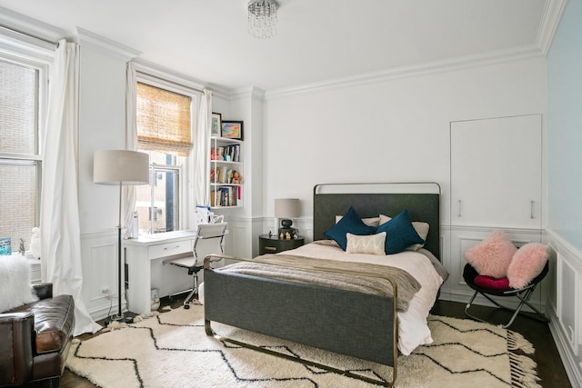 bedroom with ornamental molding, a decorative wall, wainscoting, a desk, and wood finished floors