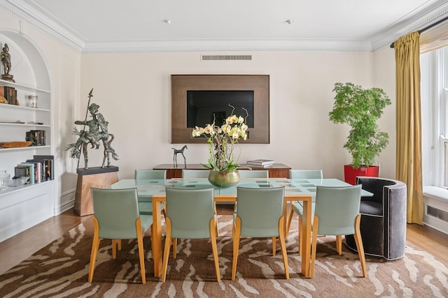 dining space featuring built in shelves, ornamental molding, and wood finished floors