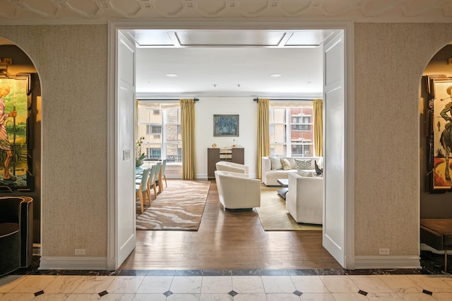 hallway with arched walkways, baseboards, wallpapered walls, ornamental molding, and wood finished floors