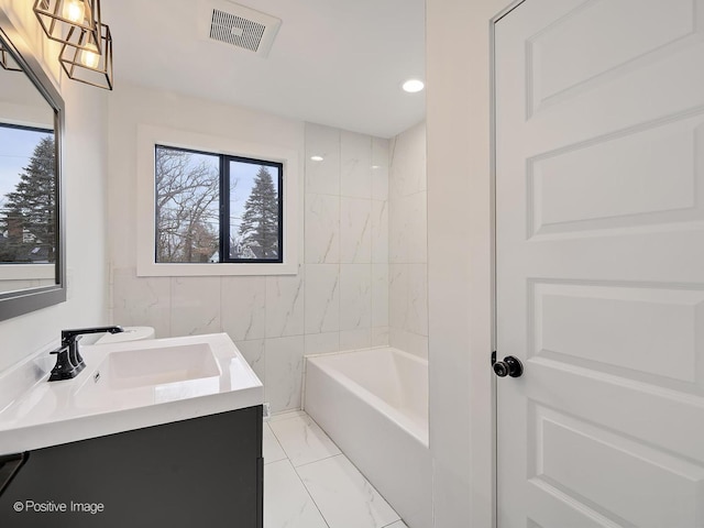 bathroom featuring marble finish floor, vanity, visible vents, and a bathing tub