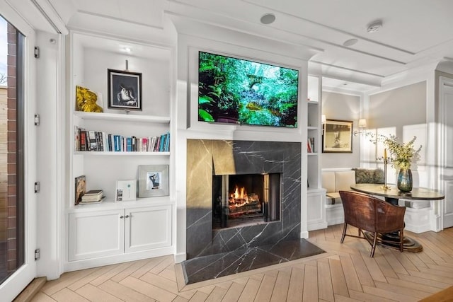 living area featuring built in shelves, light parquet flooring, and a fireplace